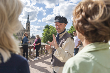 Ein Mann in Barock-Kleidung erklärt zwei Frauen etwas.