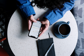 Eine Frau sitzt am Tisch und hat ein Smartphone in der Hand.