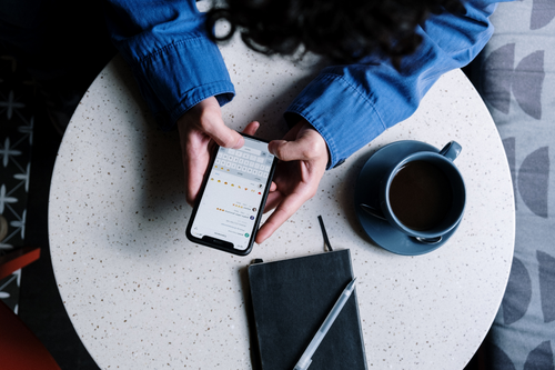 Eine Frau sitzt am Tisch und hat ein Smartphone in der Hand.